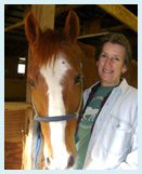 A woman standing next to a horse in a barn.